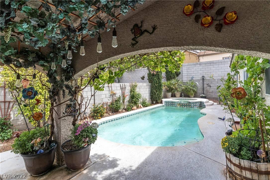 A charming outdoor area featuring a crystal clear pool and spa combinatio, covered patio, and fairy garden landscaping.